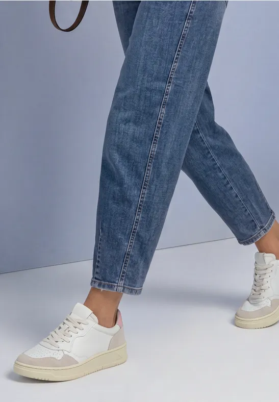 Schlichtes Outfit mit weißen Sneakers und blauen Jeans vor hellem Hintergrund
