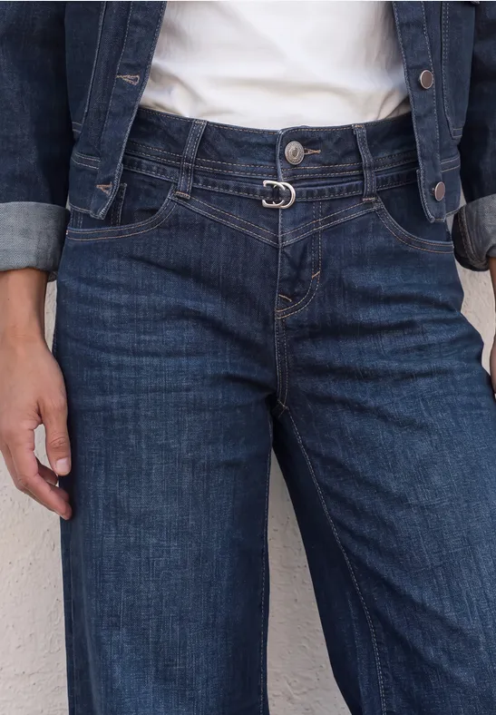 Person trägt blaue Jeanshose und Jeansjacke, Taille betont durch modische Gürtelschnalle.
