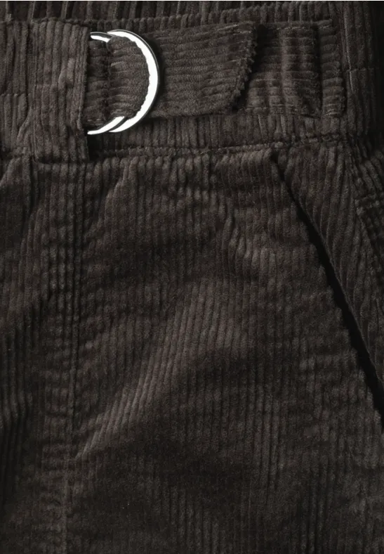 Close-up van een donkerbruine ribfluwelen broek met metalen D-ring in de taille en zijzak.
