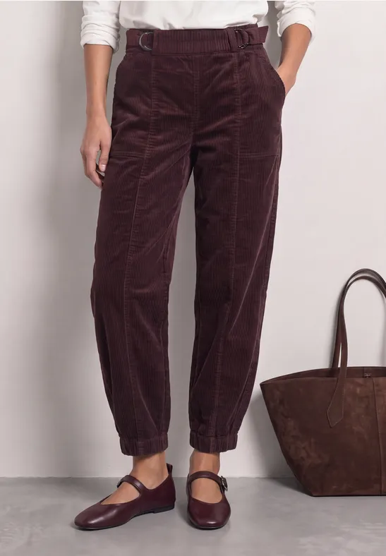 Dunkelrote Cordhose mit hohem Bund, lockerer Passform und elastischen Umschlagsäumen, kombiniert mit Mary-Jane-Schuhen.