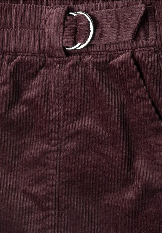 Nahaufnahme einer bordeauxroten Cordhose mit elastischem Bund, Tasche und D-Ring-Gürtel.