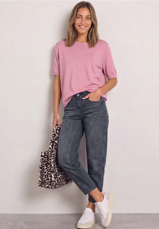 Frau in rosa Shirt, schwarzen Jeans und weißen Sneakern mit Leoparden-Tasche.