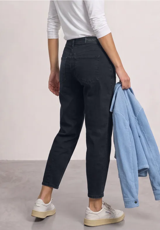 Vue de dos d’une personne en jean noir, haut blanc et baskets blanches, tenant une veste bleu clair.