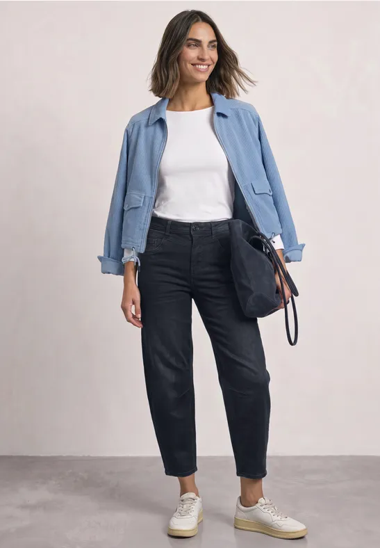 Femme portant une veste bleu clair, un tee-shirt blanc, un jean foncé, des baskets et un sac bleu marine.