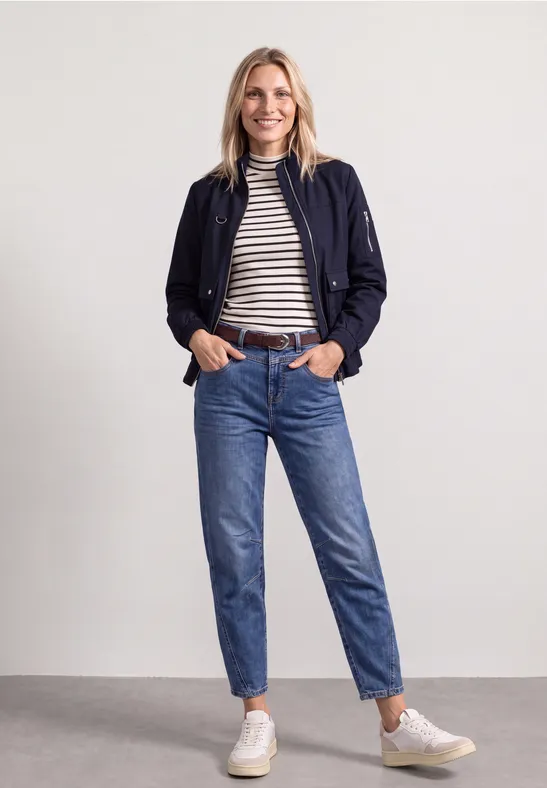 Junge Frau in lässigem Outfit mit Bomberjacke, gestreiftem Shirt, hochgeschnittener Jeans und weißen Sneakern