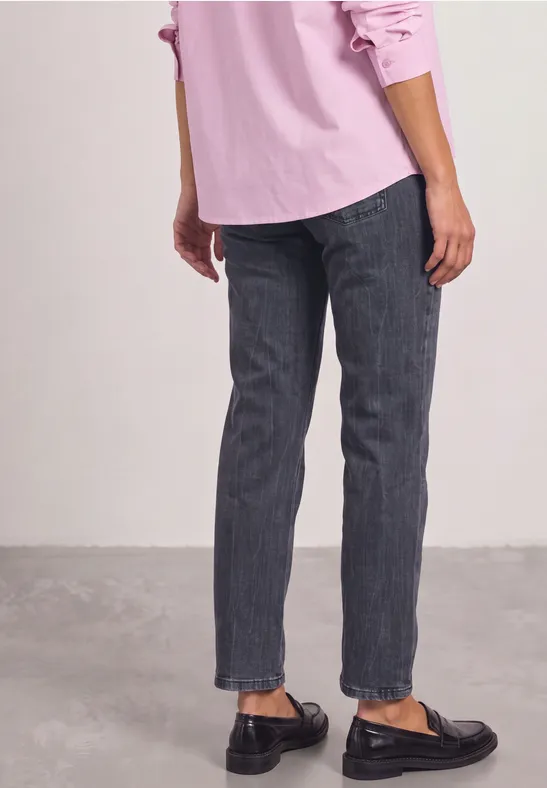Frau trägt schwarze Loafers, dunkle Jeans und rosa Hemd, seitliche Ansicht bis zu den Knöcheln