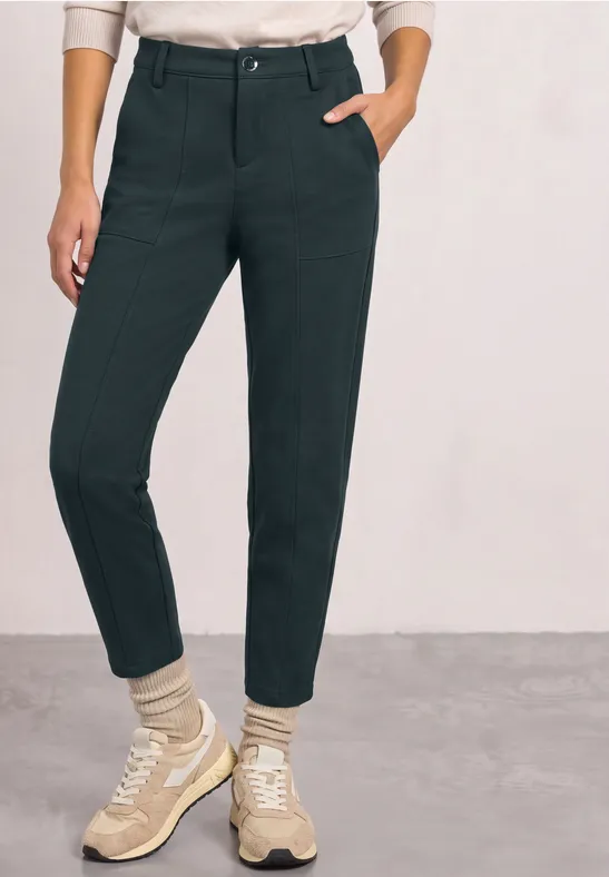 Dame trägt hoch taillierte schwarze Hose mit Eingrifftaschen, dazu helle Sneakers und Socken.