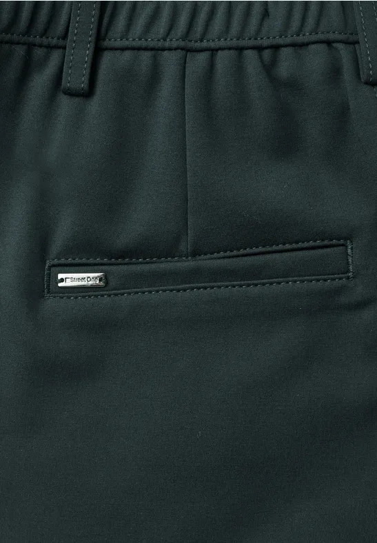 Close-up einer dunkelgrünen Hose mit elastischem Bund, Gürtelschlaufen und seitlicher Reißverschlusstasche.