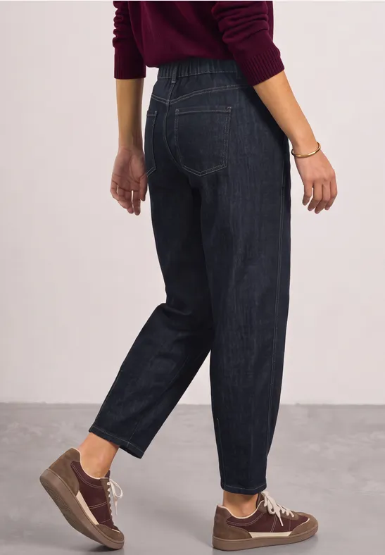 Seitlich abgelichtete Person trägt dunkelblaue Jeans, braune Sneaker und roten Pullover.