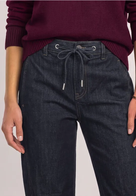 Detailaufnahme einer Frau in dunkelblauen Jeans mit Kordelzug und weinrotem Pullover.