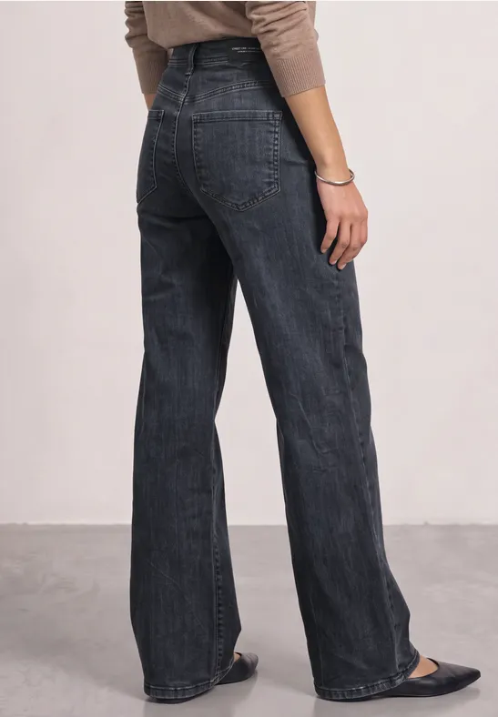 Une personne vue de dos porte un haut beige et un jean taille haute noir à coupe large.