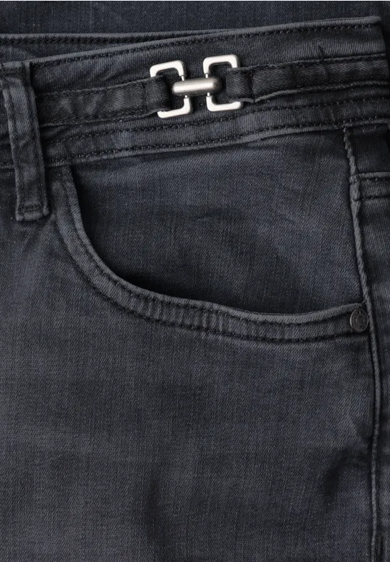 Gros plan d’un jean noir avec poche avant et petit logo métallique sur la ceinture.