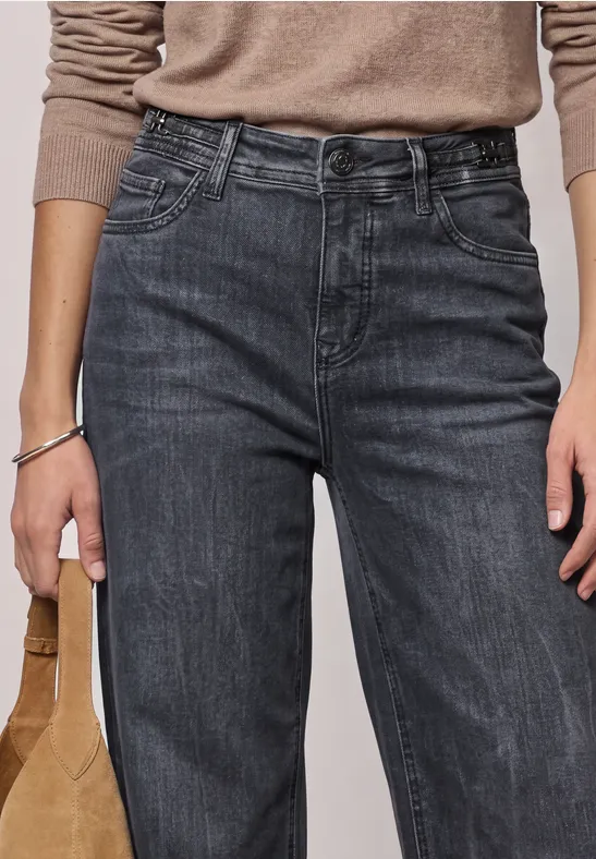 Femme portant un jean cargo noir taille haute, un top beige à manches longues et tenant un sac marron.