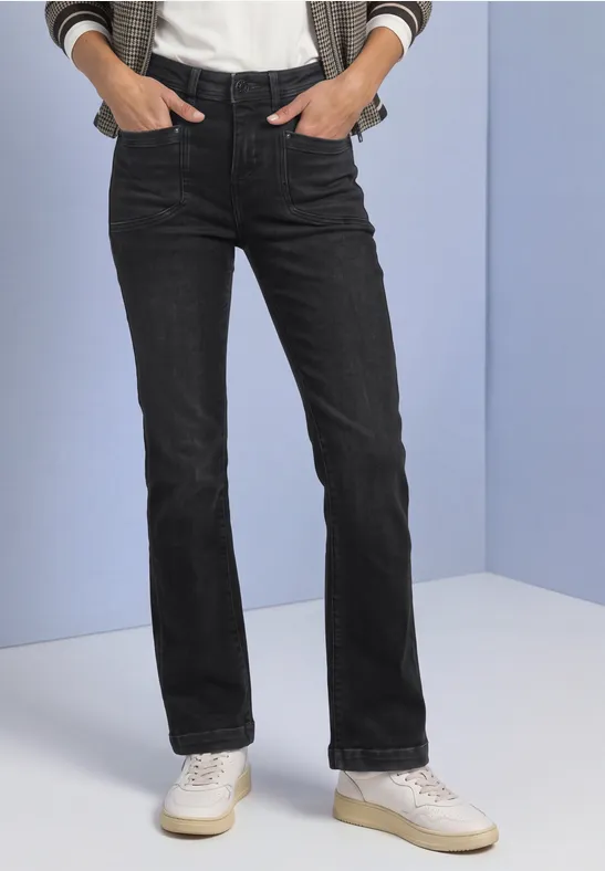 Schwarze Jeans mit geradem Schnitt und weißen Sneakern, Hände in den Taschen.