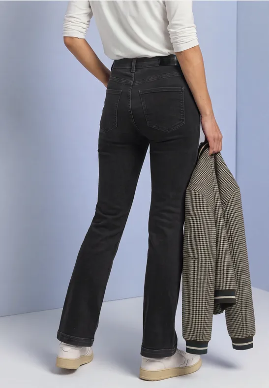 Rückansicht einer Person in schwarzer Schlaghose und weißem Oberteil, die einen karierten Blazer hält.