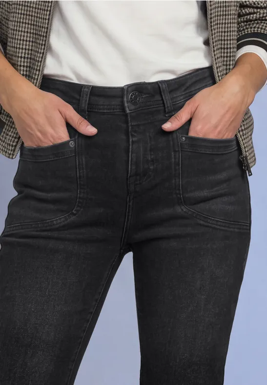 Vorderansicht einer Person mit schwarzen Jeans und kariertem Blazer, Hände in den Taschen.