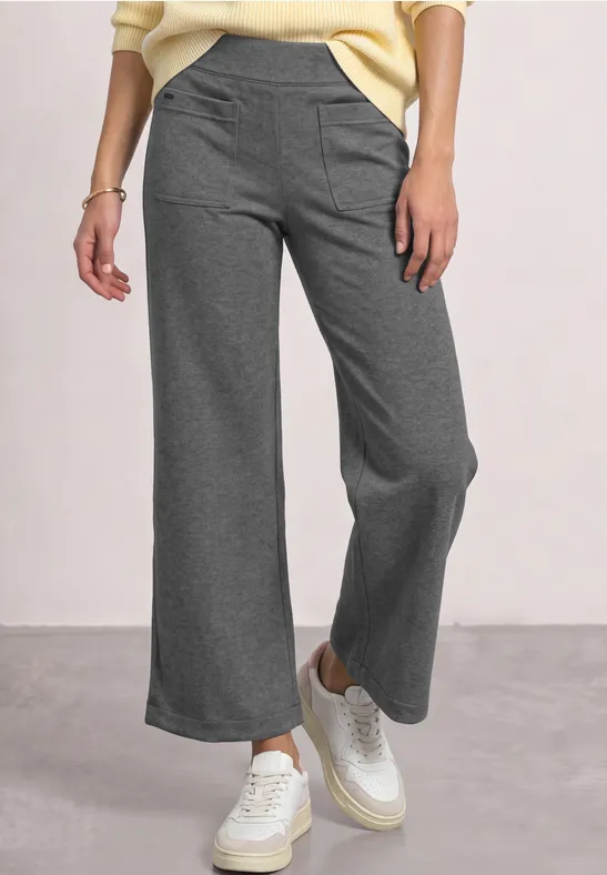 Grijze, wijde broek met hoge taille, gecombineerd met witte sneakers voor een casual uitstraling.