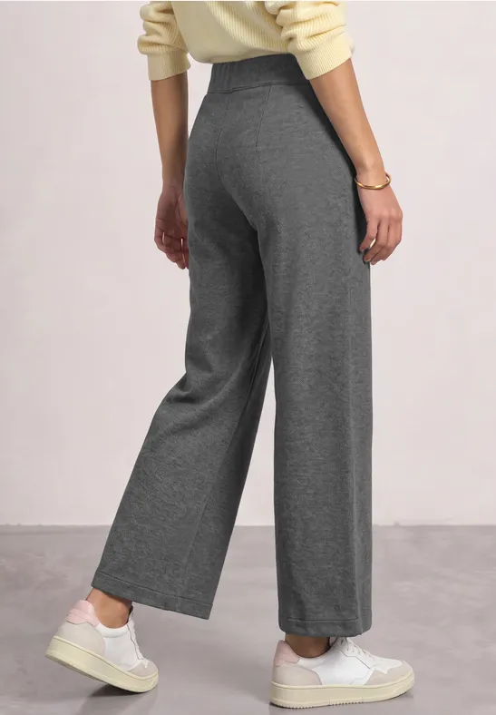 Van achteren grijze, hoog getailleerde losse broek met rechte pijpen en witte sneakers.