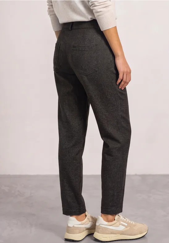 Femme vue de dos portant un pantalon gris foncé en tissu et des baskets beiges sur fond neutre.