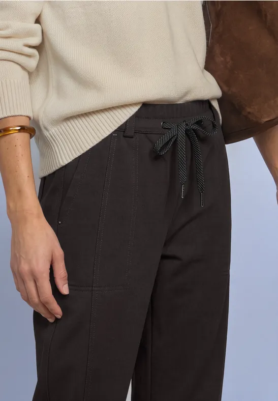 Personne en pull beige et pantalon noir taille haute à cordon et ceinture.