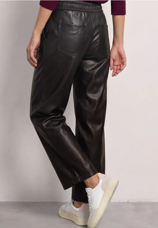 Vue arrière d’un pantalon en cuir noir taille haute à coupe droite, associé à des baskets blanches.