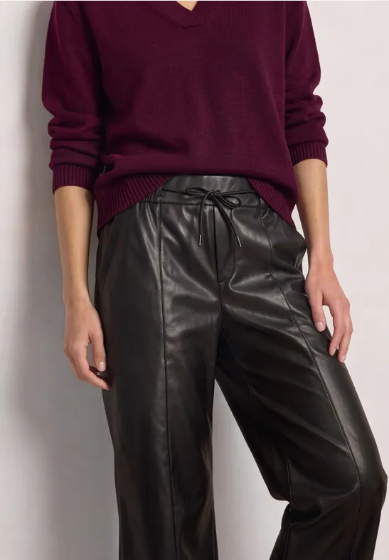 Personne en pull col V bordeaux et pantalon en cuir noir.