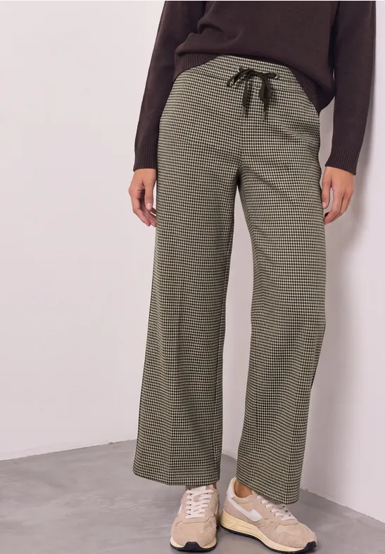 Damenhose in Olivgrün mit weitem Bein und schwarzem Kordelzug, kombiniert mit einer dunklen Oberbekleidung.