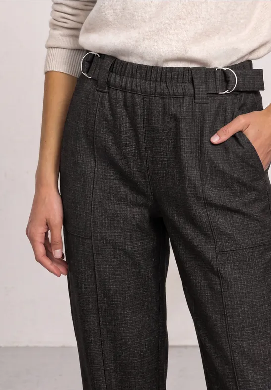 Person trägt hellen Pullover und graue karierte Hose mit elastischem Bund und D-Ring-Gürtel.