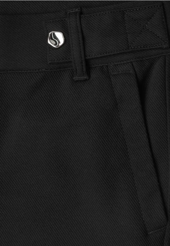 Nahaufnahme einer schwarzen Hose mit Textur, Gürtelschlaufen, seitlicher Tasche und metallischem Knopf mit Logo.
