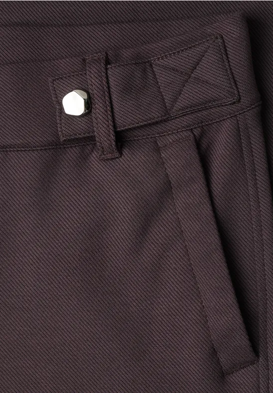 Nahaufnahme einer braunen Hose mit Bund, Gürtelschlaufe, Eingrifftasche und silbernem Knopf.