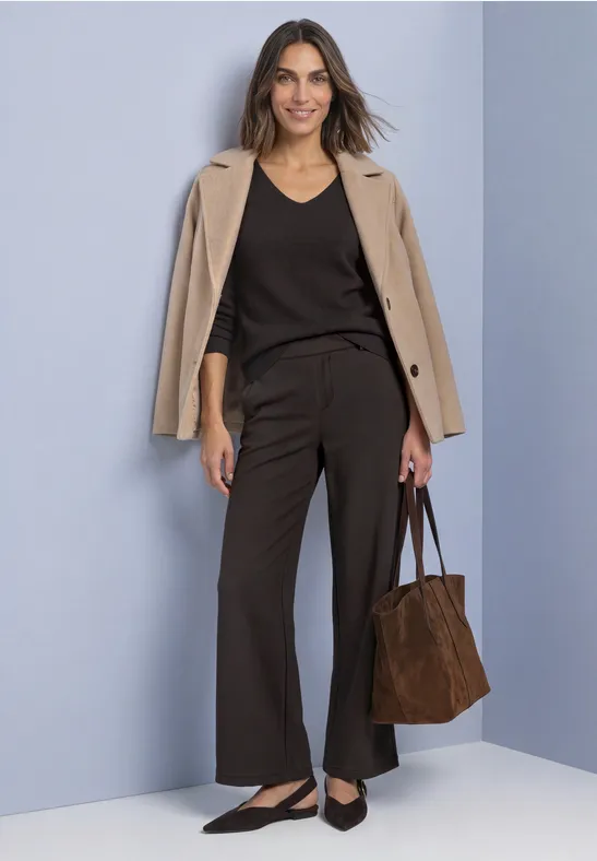 Frau in Business-Look mit beigem Blazer, schwarzem Top, weiten Hosen, Ballerinas und brauner Tasche.