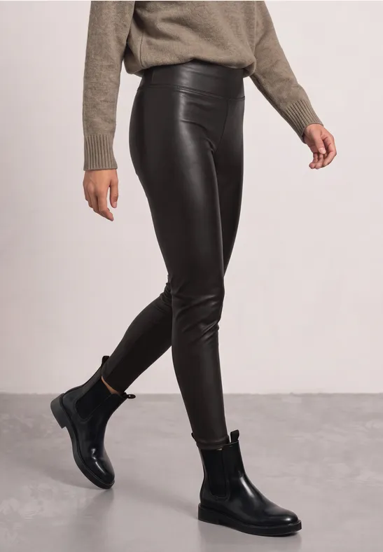 Schwarze Lederleggings und schwarze Chelsea-Boots im Studio-Setting, kombiniert mit beigem Pullover.