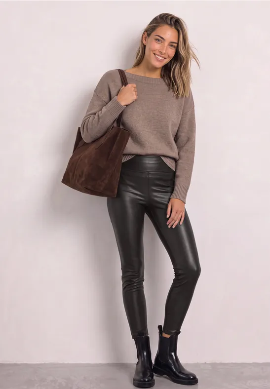 Junge Frau in lässigem Look: kuscheliger Pullover, schwarze Lederleggings, Stiefeletten und große Wildleder-Tasche.