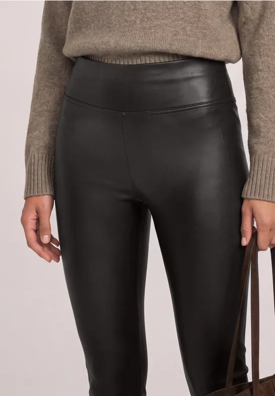 Schwarze, hochgeschnittene Lederleggings kombiniert mit grob gestricktem Pullover und Handtasche.