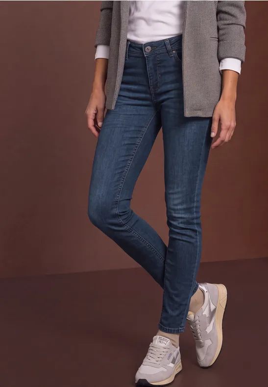 Frau trägt dunkle enge Jeans, weiße Sneakers, weiße Bluse und graue Jacke