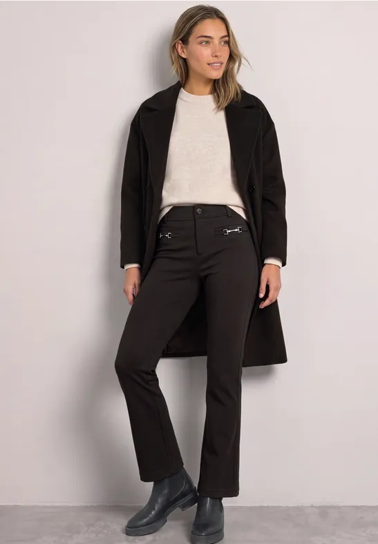 Vrouw in zwarte jas, beige trui, zwarte broek en grijze enkellaarzen.