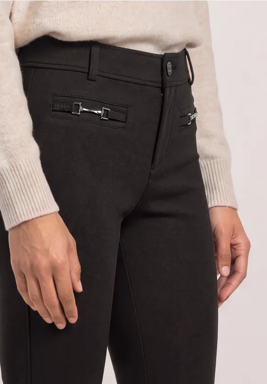 Strakke zwarte broek met zilverkleurige sierringen bij de taille, gecombineerd met een beige trui