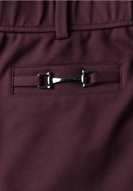 Detailaufnahme einer burgunderfarbenen Hose mit Zier-Schnalle am Gesäßtaschensaum.