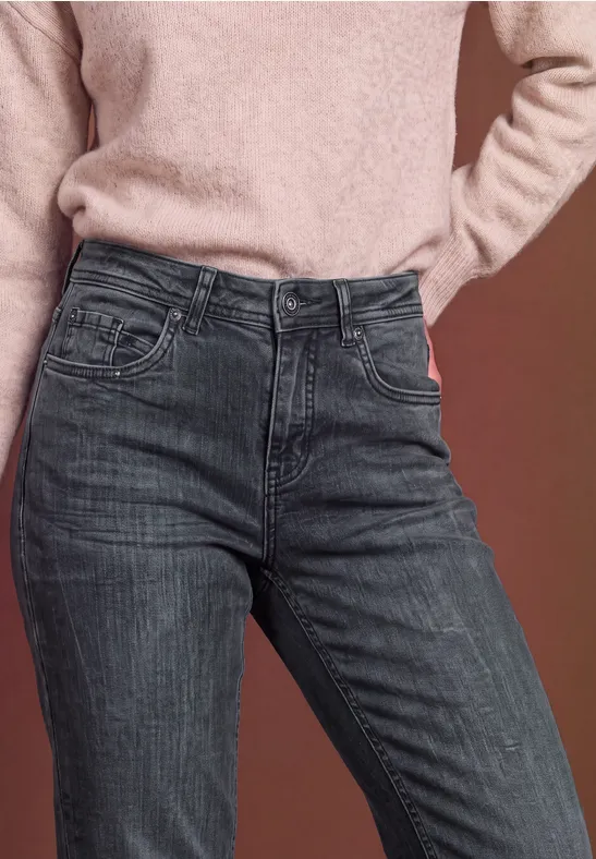 Person trägt hellen Pullover und hochgeschnittene Jeans in dunklem Washed-Look, Nahaufnahme der Taille.