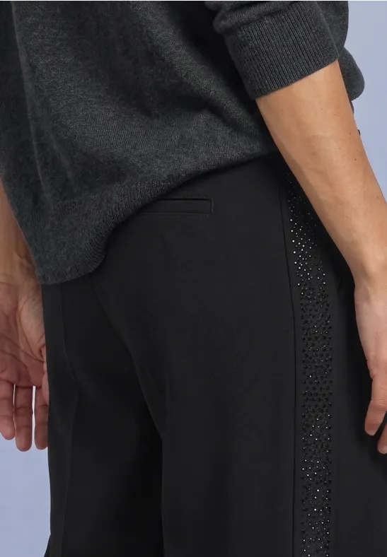 Zijaanzicht van een persoon met een zwarte broek met studdetail en een donkergrijze trui.