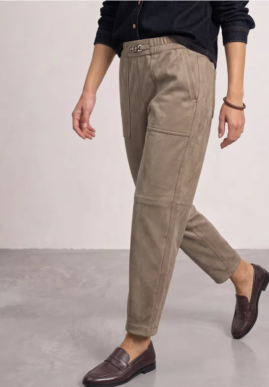 Eine Person trägt hochgeschnittene beigefarbene Cordhose mit Gürtel und dunkelbraunen Loafers.