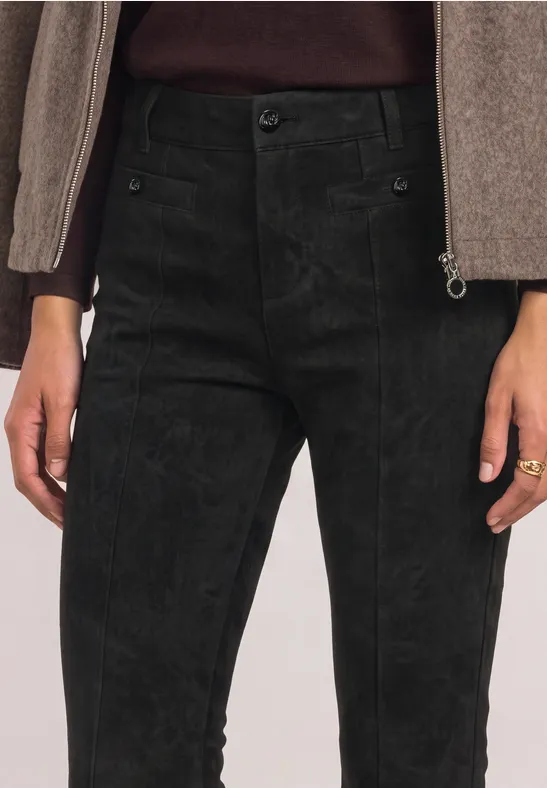 Schwarze Cordhose auf Taillenhöhe, kombiniert mit beigem Oberteil und Ring am Finger.