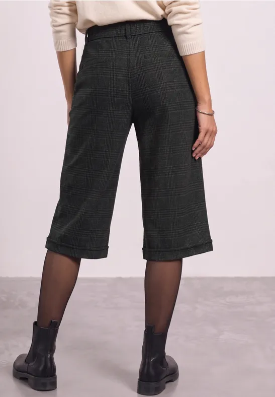 Rückansicht einer Person in weiten, midilangen grünen Culottes, schwarzen Strumpfhosen und schwarzen Boots.