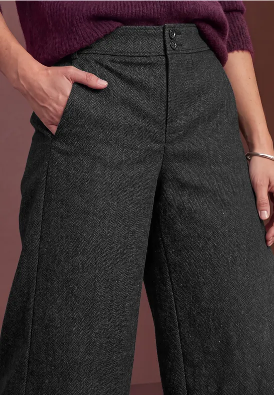 Gros plan d'une personne en pantalon gris anthracite à jambes larges, main dans la poche