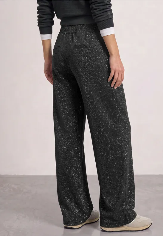 Photo d'une personne vue de dos portant un pantalon lounge ample gris foncé scintillant et des chaussons.
