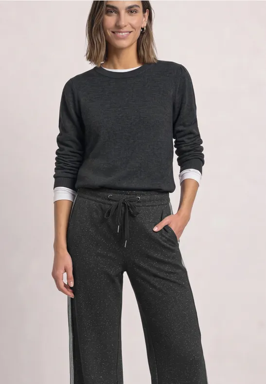 Une femme porte un pull gris foncé et un pantalon ample à cordon, look confortable et décontracté.