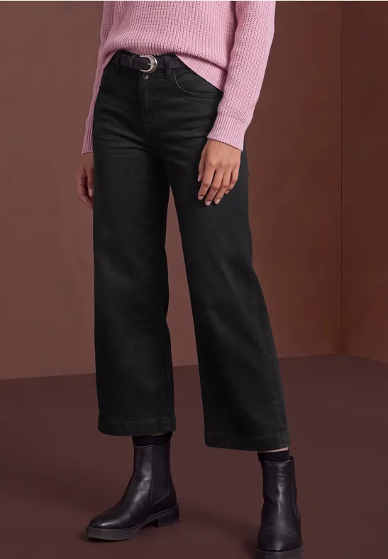 Personne portant un jean droit noir, des bottines noires et un pull rose.