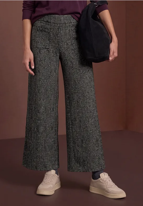 Weite, hoch sitzende graue Hose mit Textur, kombiniert mit hellen Sneakern und einer schwarzen Tasche.