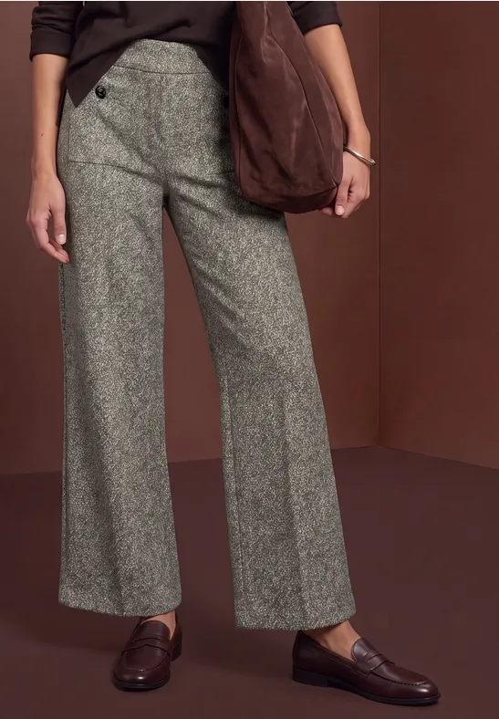 Eine Person trägt graue, weit geschnittene Hose, braune Loafers und eine lässige Schultertasche.