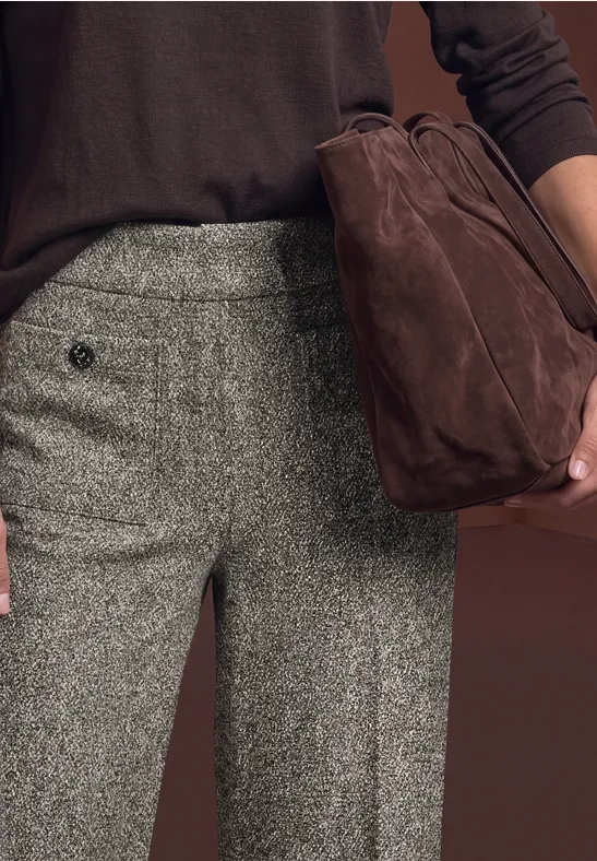 Hose aus grauem Tweed und dunkelbrauner Pullover, dazu eine braune Wildledertasche in der Hand.